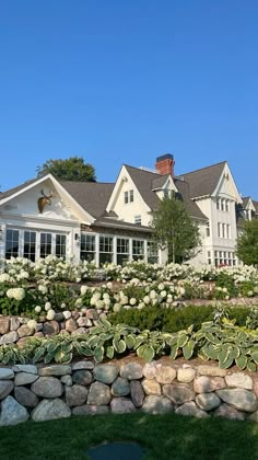 a large white house sitting on top of a lush green hillside next to a stone wall