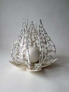 an egg sits in a white bowl on a gray surface with silver wirework around it