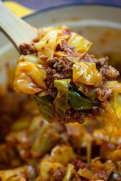 a wooden spoon full of food on top of a bowl filled with meat and vegetables