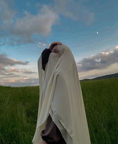 a woman standing in the middle of a field covered with a white blanket and covering her face