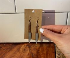 a pair of earrings is being held up by a person's hand on a wooden table