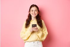 a woman in a yellow sweater is holding a cell phone and smiling at the camera