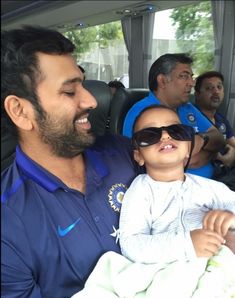 a man holding a baby in the back seat of a car with other people behind him