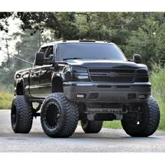 a large black truck parked on the side of a road next to some grass and trees