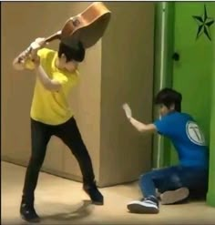 two young men are playing with each other in front of a green wall and one is holding a baseball bat