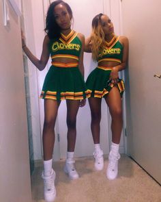 two girls in green and yellow cheerleader outfits standing next to each other with their hands on their hips