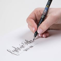 a woman's hand writing on a piece of paper with a black ink pen