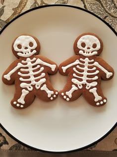 two decorated cookies in the shape of skeletons on a plate