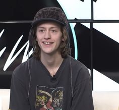 a young man wearing a hat sitting in front of a wall with an advertisement on it