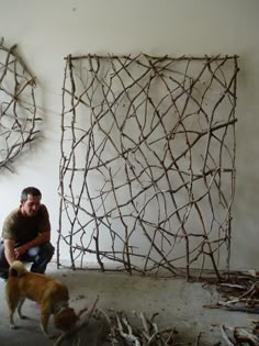 a man sitting next to a dog in front of a sculpture made out of sticks