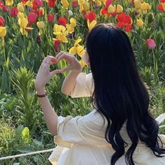 a woman sitting in front of flowers making a heart shape with her hands while looking at the tulips