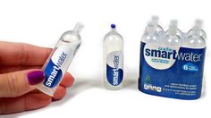 a hand is holding a small plastic bottle with water in it and two bottles next to it