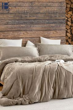 a bed covered in blankets and pillows next to a pile of wood with logs behind it