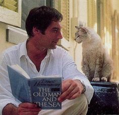 a man reading a book next to a cat