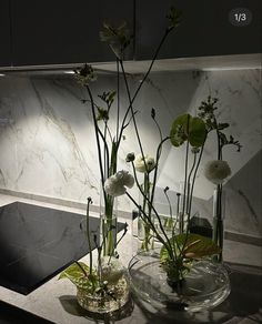 two clear vases with flowers in them on a marble countertop next to a sink