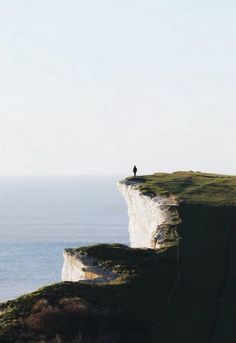 a lone person standing on the edge of a cliff overlooking the ocean and cliffs below