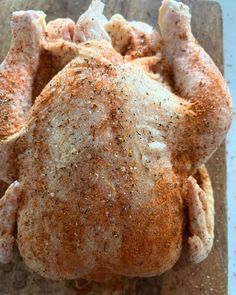 a whole chicken sitting on top of a wooden cutting board with seasoning sprinkled around it