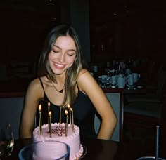 a woman sitting at a table in front of a pink cake with candles on it