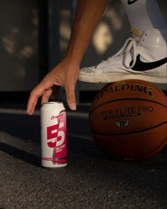 a person reaching for a basketball on the ground next to a can of energy drink