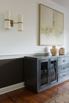 a painting hangs on the wall next to a black cabinet with two white vases