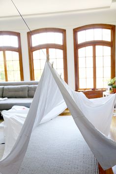 a hammock hanging from the ceiling in a living room with two large windows