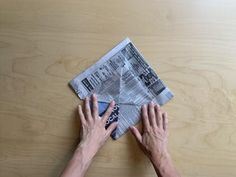 two hands reaching for a piece of newspaper on top of a wooden table with wood grained surface