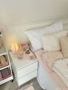 a white bed topped with lots of pillows next to a night stand filled with pink flowers