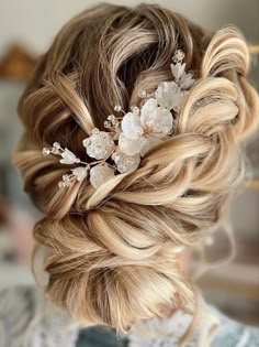 a woman with blonde hair and flowers in her hair is wearing a braided updo