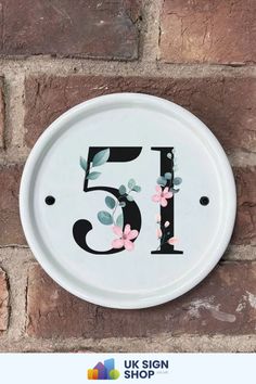 a white sign with flowers on it that says 5 in front of a brick wall