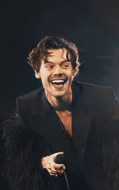 a man in a black suit laughing and holding a microphone