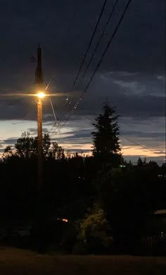 the street light is shining brightly in the dark night sky above some power lines and trees