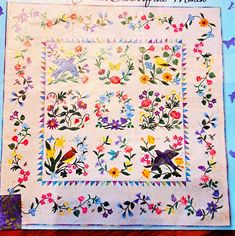 an old quilt with birds and flowers on it, sitting on top of a table