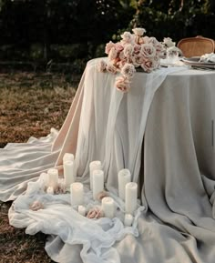 a table with candles and flowers on it in the middle of an open field at sunset