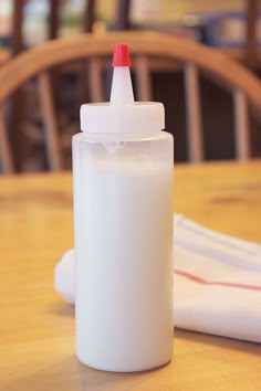 a bottle with a red cap sitting on top of a table next to a napkin