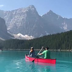 two people in a red canoe paddling on the water with mountains in the background