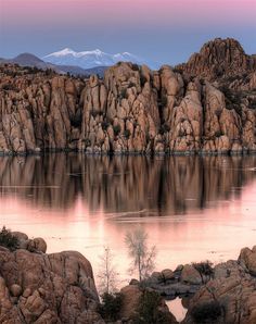 a lake surrounded by rocks and mountains with water in the foreground at sunset or dawn