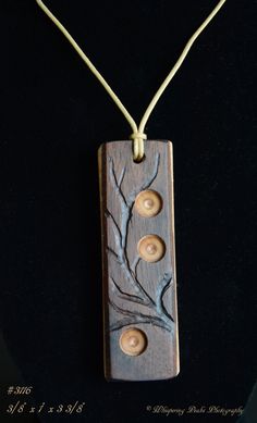 a wooden pendant with three buttons and leaves on it's back drop down from the necklace