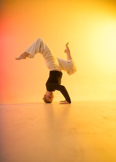 a person doing a handstand on the floor in front of an orange and yellow background