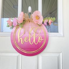 a pink door hanger with the word hello painted on it and flowers in front