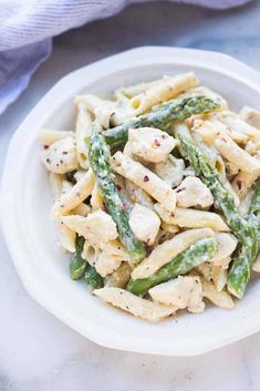 a white bowl filled with pasta and asparagus on top of a marble table