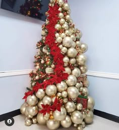 a christmas tree made out of balls and ornaments in an office cubicle with a red ribbon on the top