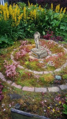 a small statue in the middle of a garden with flowers and plants around it's edges