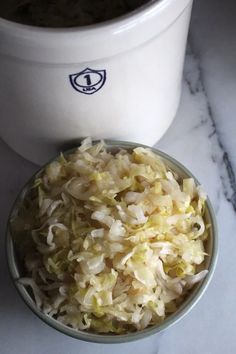 a bowl filled with shredded cabbage next to a white cup on a marble counter top