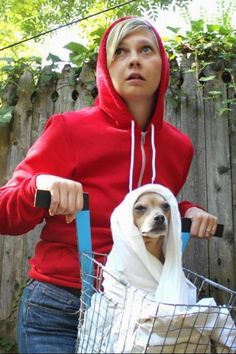 a woman in a red hoodie riding a bike with a dog wrapped in a blanket