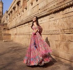 a woman standing in front of a stone wall wearing a long dress and posing for the camera