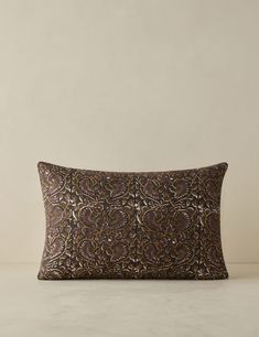 a brown and black decorative pillow on a white surface with a beige wall in the background