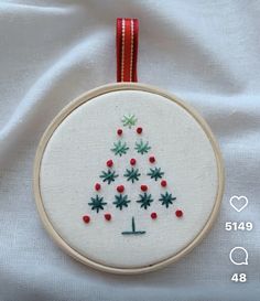 a cross stitch christmas tree ornament hanging from a red ribbon on a white sheet