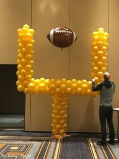 a man standing next to a giant balloon shaped like the letter h with a football on it