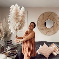 a woman in an orange dress is holding a large feather ball and standing next to a black leather couch