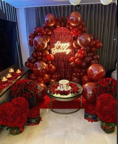 a birthday cake surrounded by red flowers and balloons in front of a large balloon arch